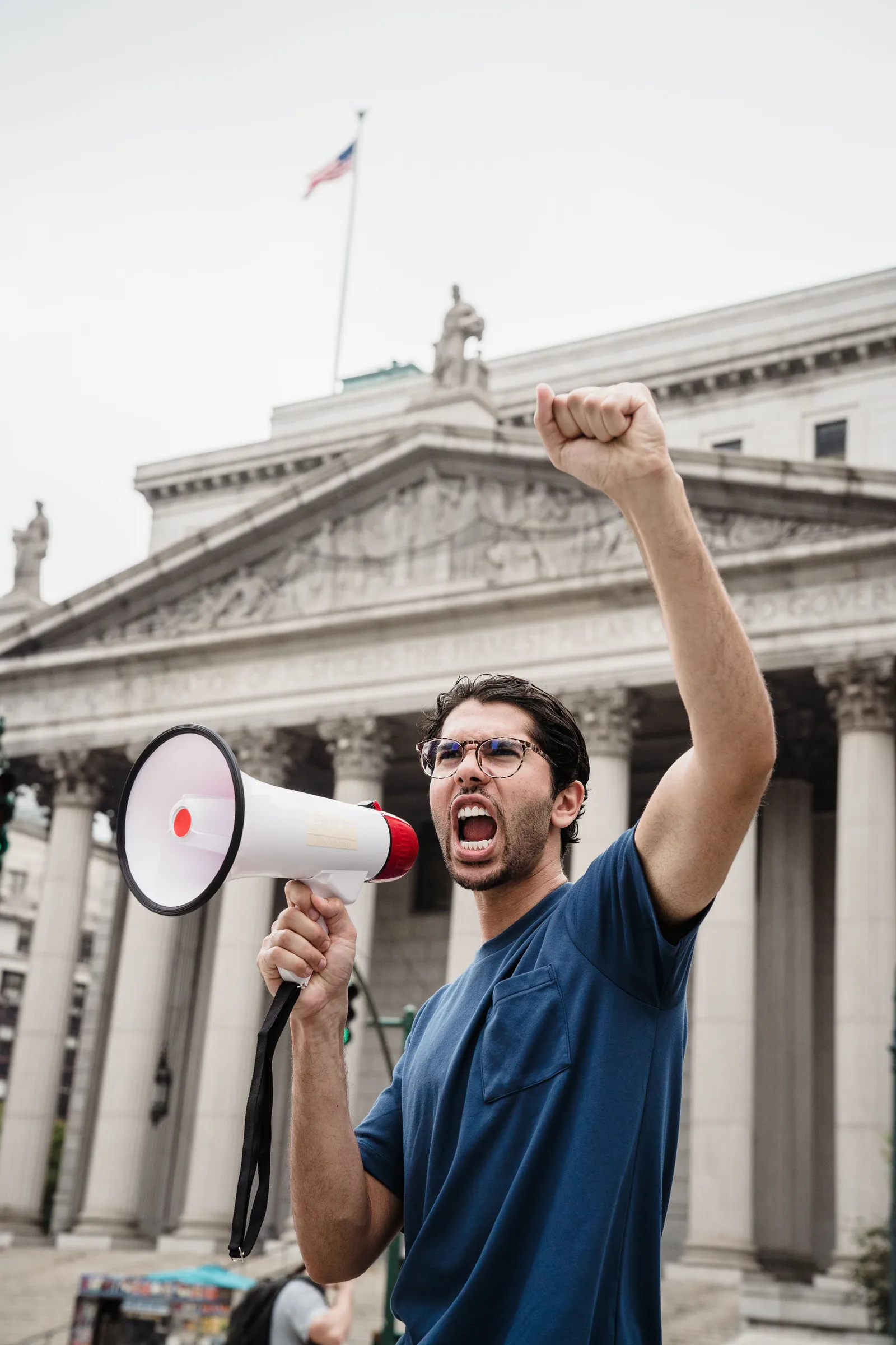A man raises his fist and speaks through a megaphone outside a government building