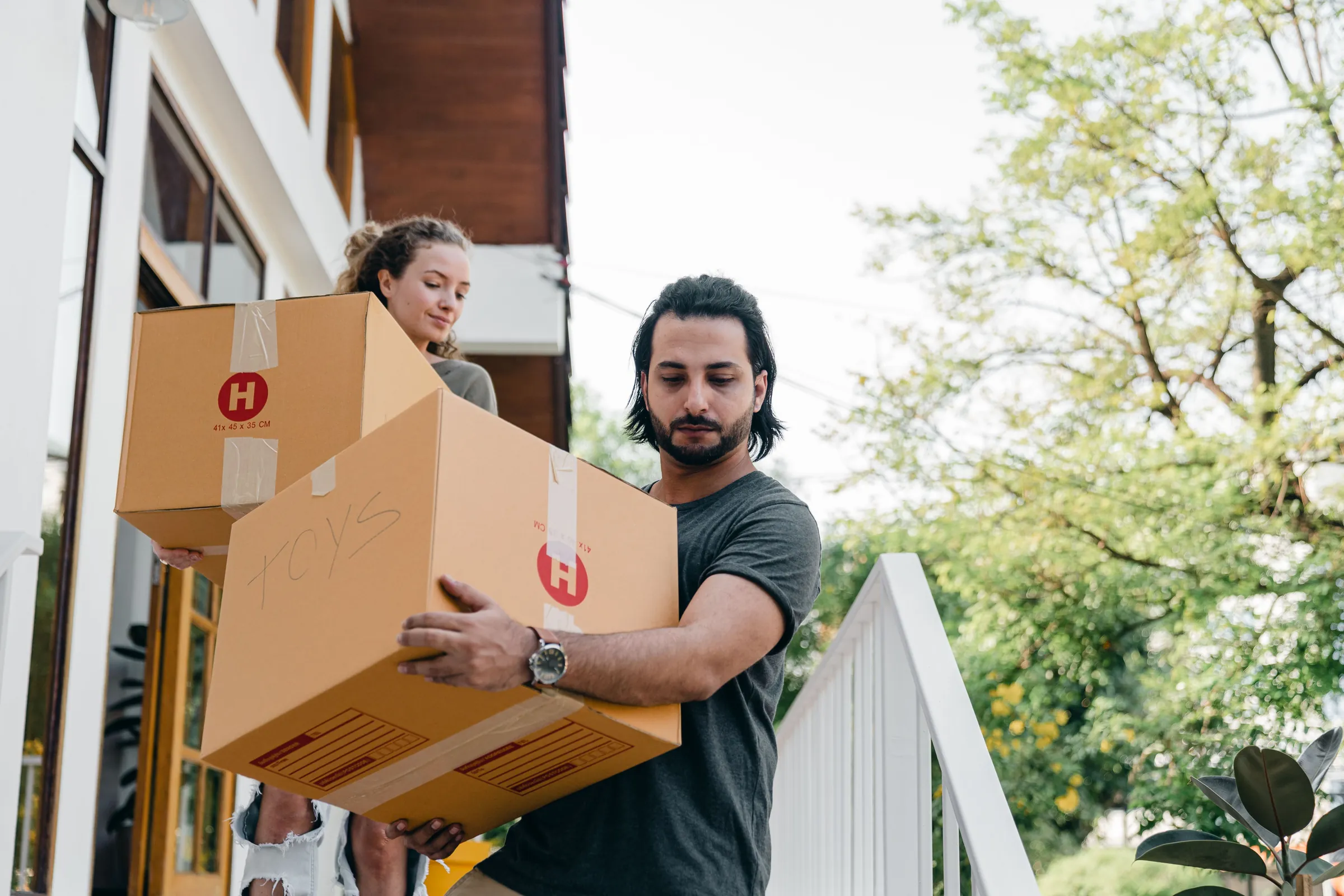 A young couple carries moving boxes into a home