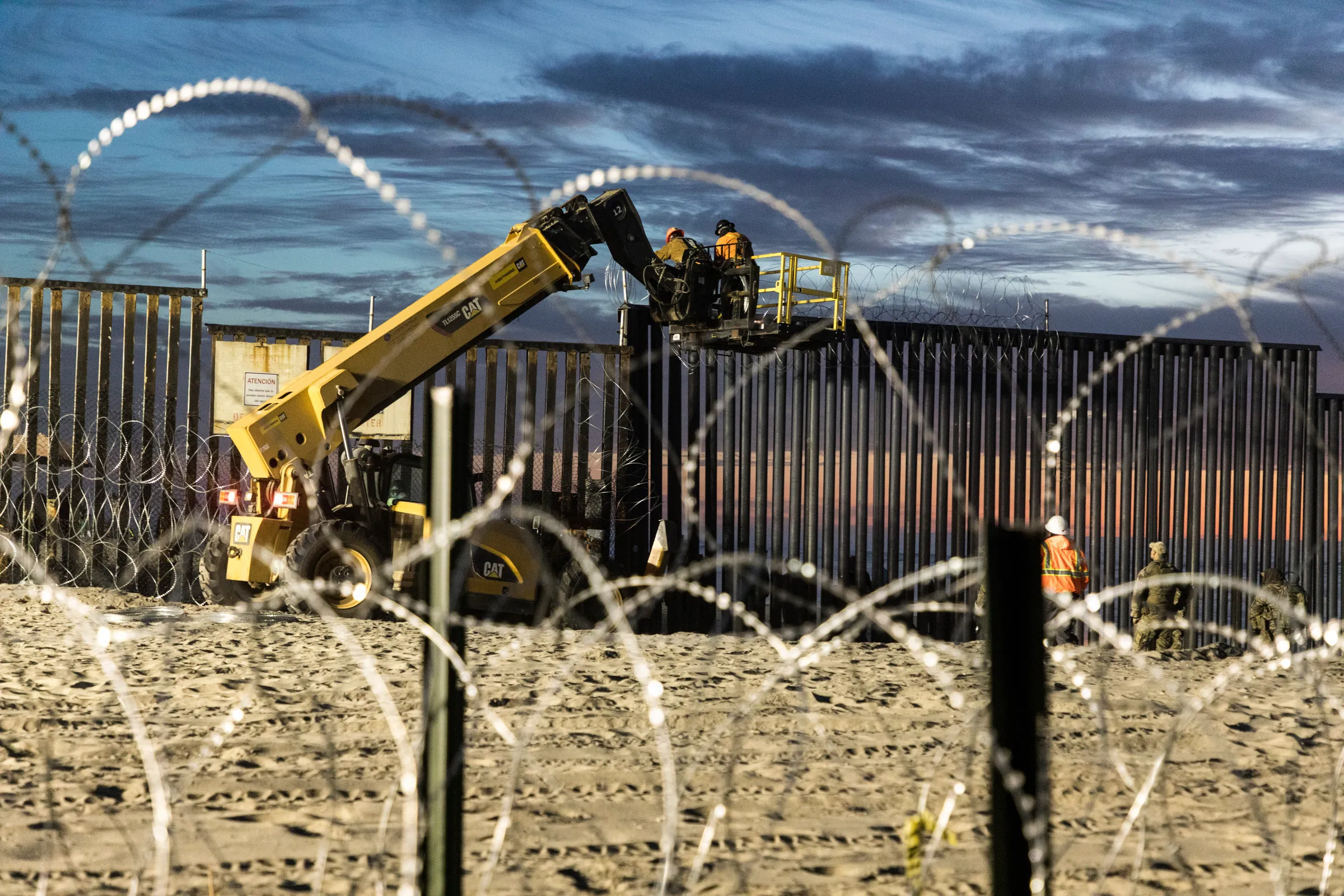 Border Patrol agents stand watch as crews reinforce the U.S.-Mexico border wall at dusk
